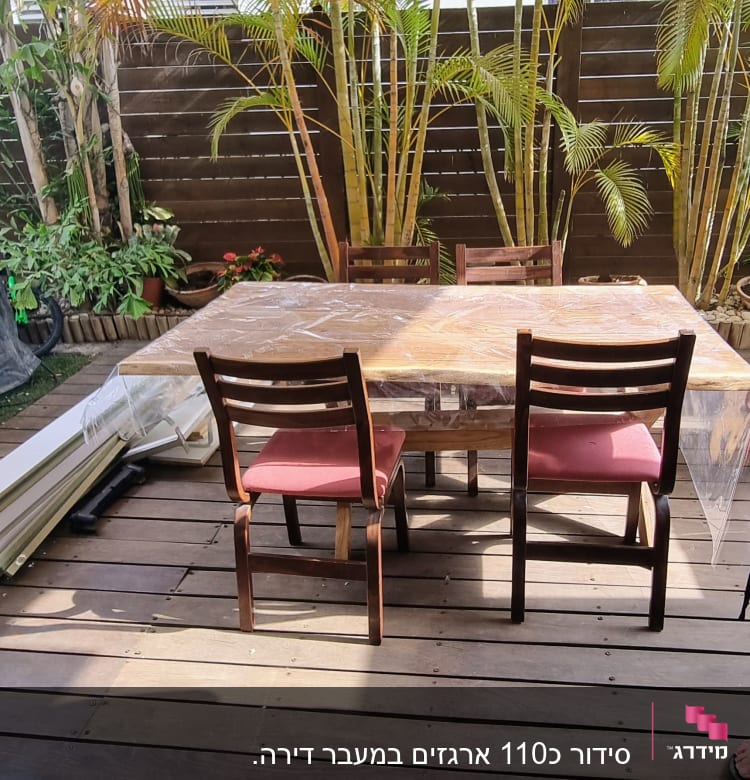 שולחן עץ עם כיסאות במרפסת, צמחים ברקע